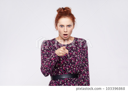 Portrait of extremely astonished ginger woman wearing dress pointing at camera, being very shocked to choose you, keeps mouth open. Indoor studio shot isolated on gray background. 103396868