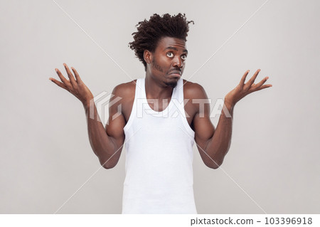 I dont know this. Portrait of confused puzzled man with Afro hairstyle feels uncertain as cant find right way, wearing white T-shirt. Indoor studio shot isolated on gray background. 103396918