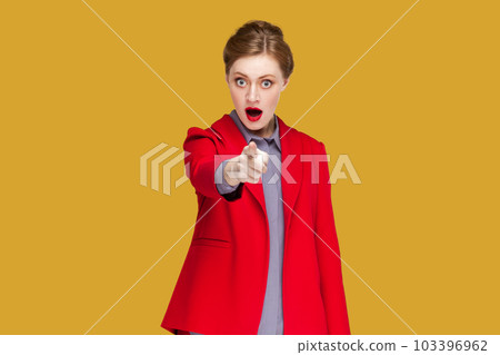 Portrait of shocked astonished woman with red lips standing indicating fore finger to you, being amazed and surprised, choosing you, wearing jacket. Indoor studio shot isolated on yellow background. 103396962