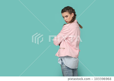 Portrait of upset teenager girl with braids wearing pink jacket turning to camera with sad look, looking at camera, expressing sorrow and sadness. Indoor studio shot isolated on green background. 103396968
