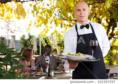 Adult waiter who is standing with order at summer cafe Adult waiter who is standing with order at summer cafe 103397297