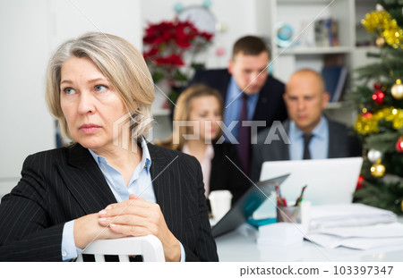Upset mature woman at office on background with coworkers Upset mature woman at office on background with coworkers 103397347