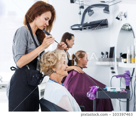 Hairdresser making hairstyle for elderly female 103397463