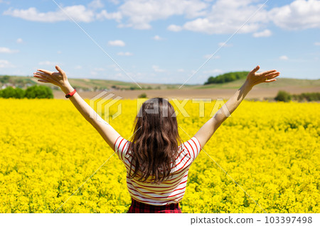 A girl stands in the middle of a beautiful rapeseed field with a beautiful blue sky. Biofuel concept. 103397498