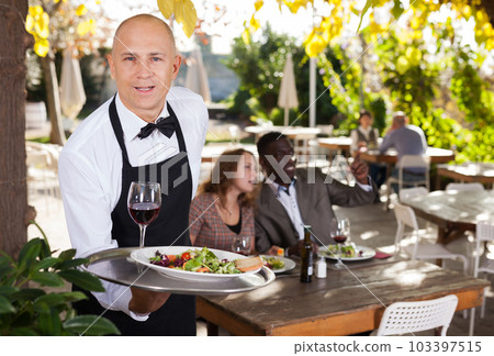 Adult waiter who is standing with order at summer cafe Adult waiter who is standing with order at summer cafe 103397515