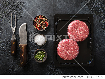 Raw beef burgers sealed in vacuum tray with barbeque fork and knife 103397718