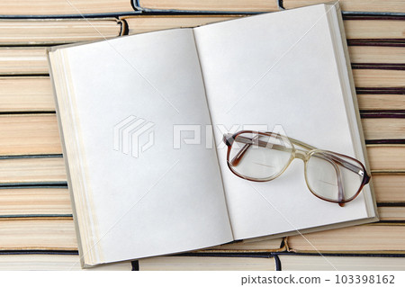 An open vintage book or notebook with blank pages and reading glasses on the background of a row of shabby books 103398162