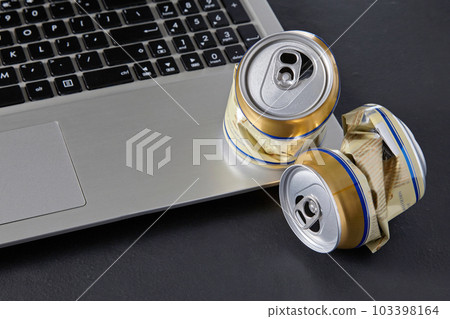 Empty crumpled beer cans on a laptop keyboard on a black backgro 103398164