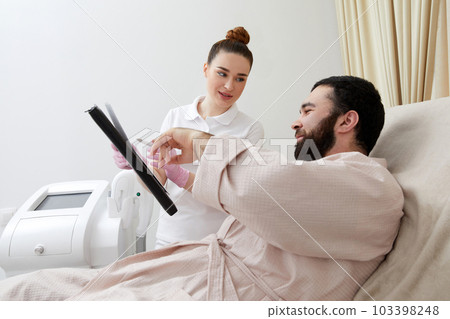 Professional cosmetician woman with papers talking to man before procedure in clinic of esthetic cosmetology 103398248
