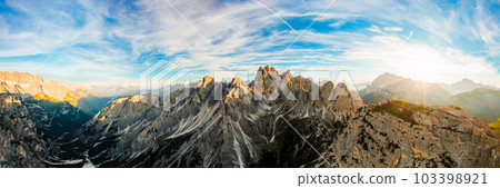 Mountain landscape at sunrise. Rising sun rays illuminate stony treeless slopes of Three Peaks of Lavaredo under clear sky aerial view in back lit Mountain landscape at sunrise. Rising sun rays illuminate stony treeless slopes of Three Peaks of Lavaredo under clear sky aerial view in back lit 103398921