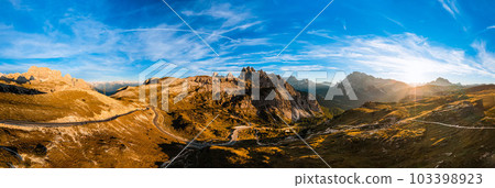 High stone columns of mountain massif of Tre Cime di Lavaredo at sunset. Battlement-like peaks under blue sky with white clouds aerial view 103398923