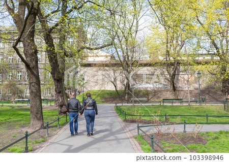 [波蘭]一對老年夫婦在克拉科夫老城公園的綠樹成蔭的街道上行走 103398946