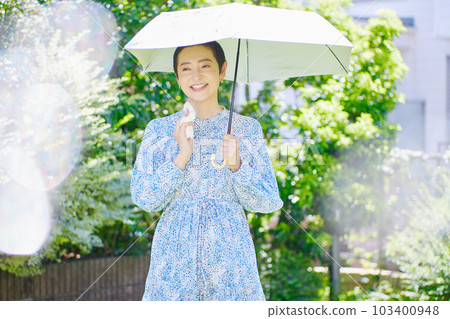 一位中年婦女在夏日的陽光下打著陽傘行走 103400948