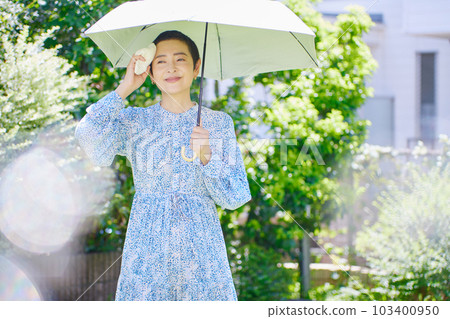 A middle-aged woman walking with a parasol in the summer sun A middle-aged woman walking with a parasol in the summer sun 103400950