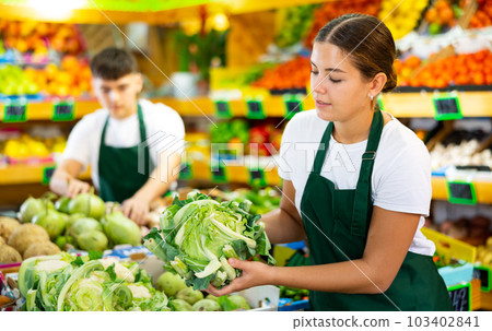 Friendly young seller woman in apron demonstrating cauliflower in shop 103402841