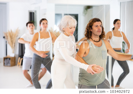 Dancer man learn ballet elements with choreographer during group training at hall. Dancer man learn ballet elements with choreographer during group training at hall. 103402972