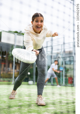 Sportive young woman playing padel with partner outdoors. View through tennis net 103402976