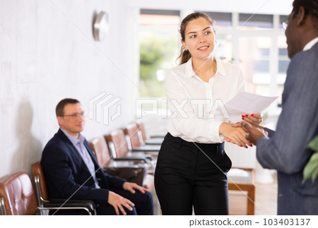 Young woman handshaking with other person in waiting room Young woman handshaking with other person in waiting room 103403137
