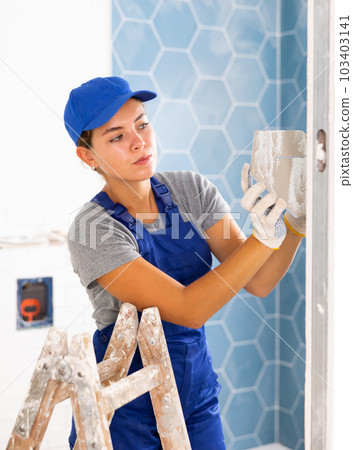 Young woman tiler glues ceramic tiles on the wall Young woman tiler glues ceramic tiles on the wall 103403141