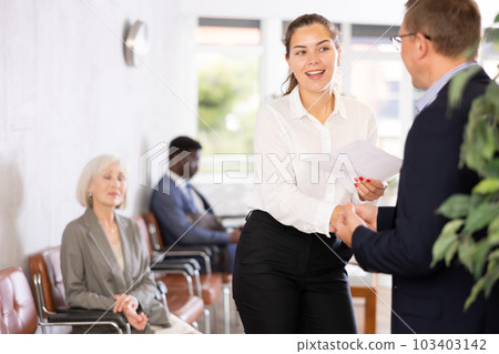 Young woman handshaking with other person in waiting room Young woman handshaking with other person in waiting room 103403142