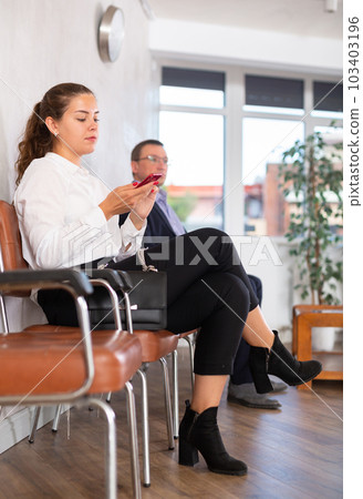 Young female visitor sitting on the bench in waiting room of clinic Young female visitor sitting on the bench in waiting room of clinic 103403196