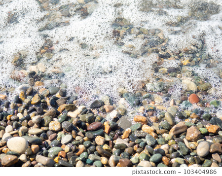 Wave on a pebbly shore. Sea foam. Beautiful pebble beach. Close-up of the coastline Wave on a pebbly shore. Sea foam. Beautiful pebble beach. Close-up of the coastline 103404986
