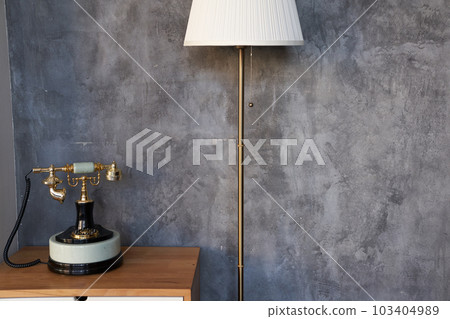 A close-up of an antique telephone and a white floor lamp against a concrete wall, ideal for reading in the living room. With a space to copy. High quality photo A close-up of an antique telephone and a white floor lamp against a concrete wall, ideal for reading in the living room. With a space to copy. High quality photo 103404989