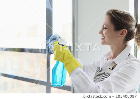 Cheerful maid sprays detergent on window glass in hotel room Cheerful maid sprays detergent on window glass in hotel room 103406097