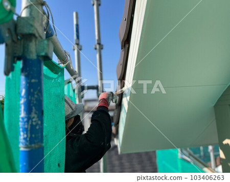 A male painter brushes gables on scaffolding at a detached house renovation painting site A male painter brushes gables on scaffolding at a detached house renovation painting site 103406263