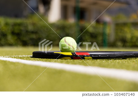Close-up of tennis racket and ball by white marking on grassy field at tennis court 103407140