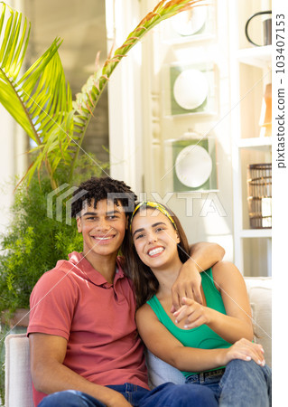 Portrait of smiling biracial young boyfriend with girlfriend relaxing on sofa in living room 103407153