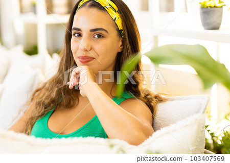 Close-up portrait of biracial young woman with hand on chin relaxing on sofa in living room 103407569