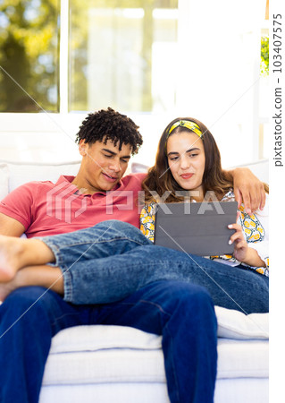 Biracial young couple using digital tablet while relaxing on sofa in living room 103407575