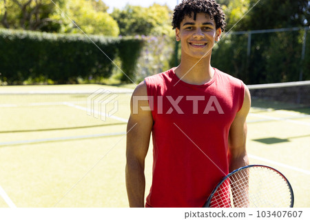 Portrait of smiling biracial young man holding tennis racket while standing in court Portrait of smiling biracial young man holding tennis racket while standing in court 103407607