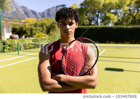 Portrait of biracial young man with arms crossed holding tennis racket while standing in court Portrait of biracial young man with arms crossed holding tennis racket while standing in court 103407608