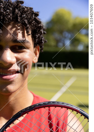 Close-up portrait of biracial young man with tennis racket smiling in tennis court on sunny day 103407609