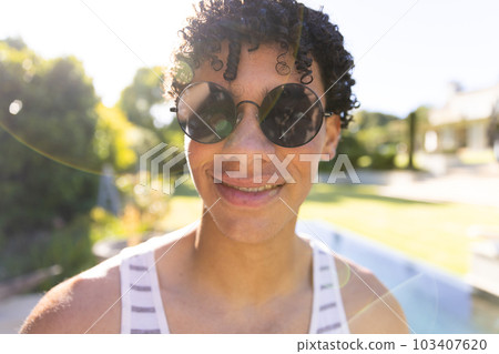 Close-up portrait of smiling biracial young man wearing sunglasses and posing in yard 103407620