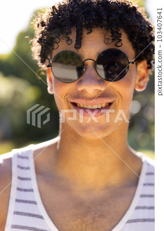 Close-up portrait of smiling biracial young man wearing sunglasses in yard on sunny day 103407641