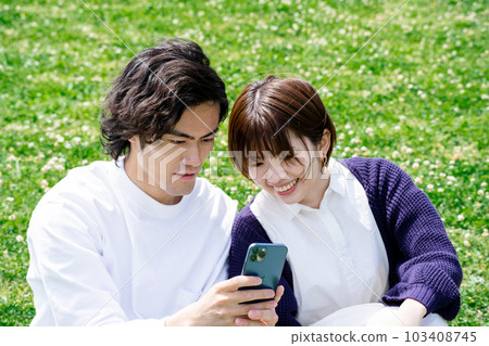 A couple looking at a smartphone in the green A couple looking at a smartphone in the green 103408745