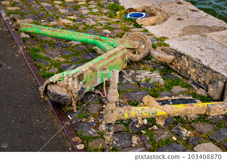 Rental electric scooters covered in mud and garbage on embankment.  103408870