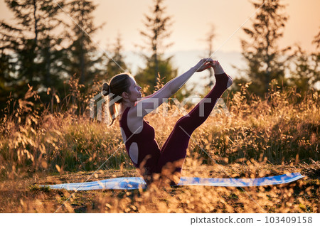 Sporty girl doing boat pose. Young female doing yoga exercises at dawn. Practicing yoga on fresh air. 103409158