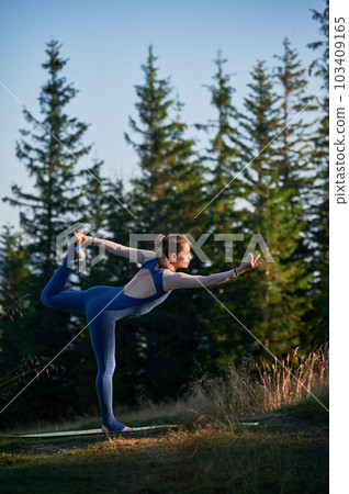 Young woman doing yoga asana Natarajasana. Sporty girl doing lord of the dance pose. Practicing gymtastic outdoor. 103409165