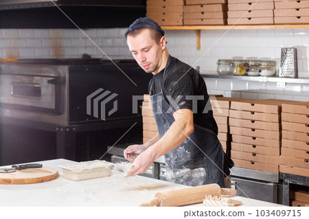 Dough for pizza, the chef rolls out the blanks. Closeup hand of chef baker in uniform white apron cook pizza at kitchen 103409715
