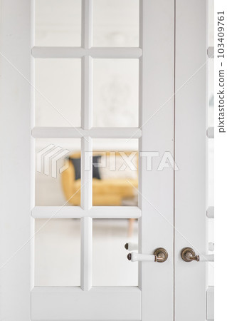 Old-style door, white - handle close up. The interior of a bright living room in a modern apartment. 103409761