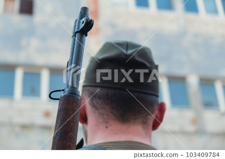 Back view of unrecognizable man in body armor during war weapon. Soldier hold the gun next to building wall. War preparation Back view of unrecognizable man in body armor during war weapon. Soldier hold the gun next to building wall. War preparation 103409784