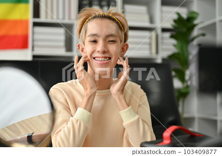 A young Asian gay man is massaging his face, applying his face serum 103409877
