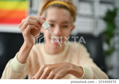 A young Asian gay man dropping facial essential serum on his hand, applying skincare 103409878