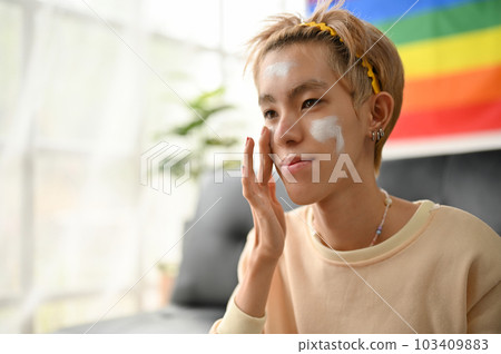 A happy young Asian gay man is applying sunscreen or moisturizer on his face A happy young Asian gay man is applying sunscreen or moisturizer on his face 103409883