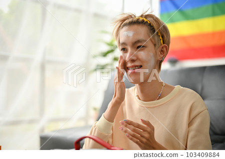 A happy young Asian gay man is applying facial treatment moisturizer cream 103409884