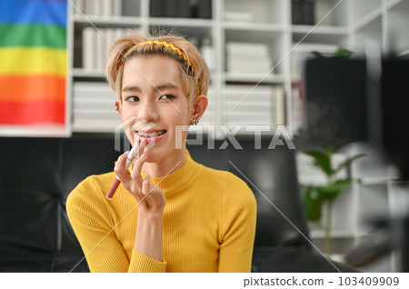 An attractive young Asian gay beauty blogger applying lipstick to his lip, talking to the camera 103409909